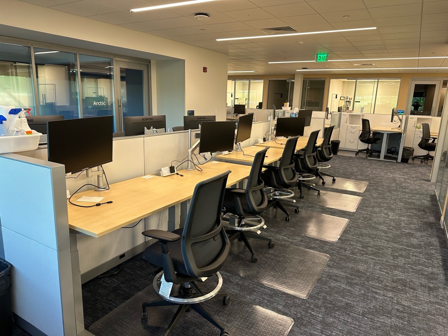 Modern office space with ergonomic chairs and workstations featuring desktop monitors, arranged in a clean, open-plan layout.